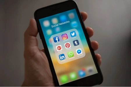 A hand holding a phone that displays various social network apps