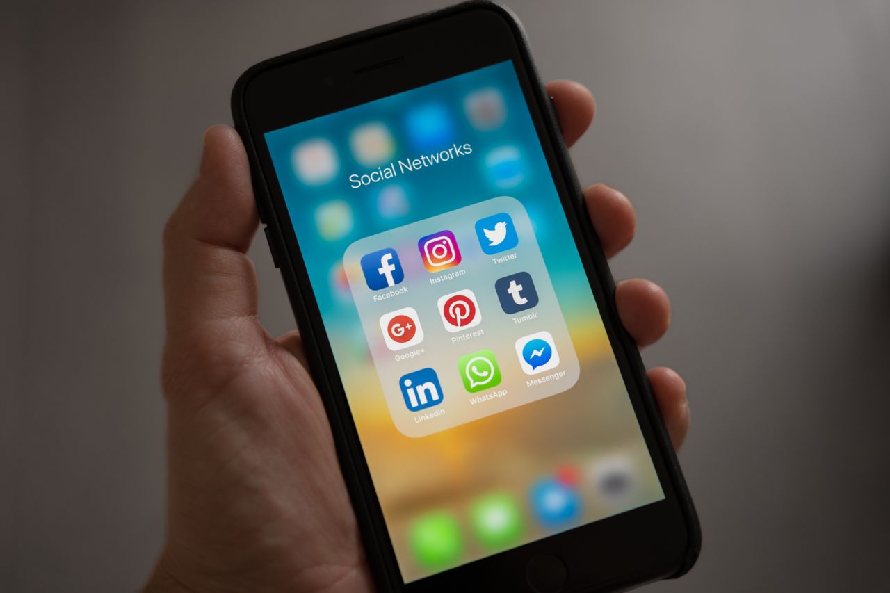 A hand holding a phone that displays various social network apps
