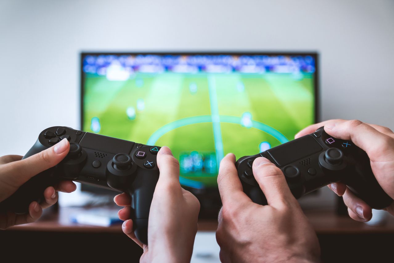 Close-up of hands holding Playstation controllers in front of a tv