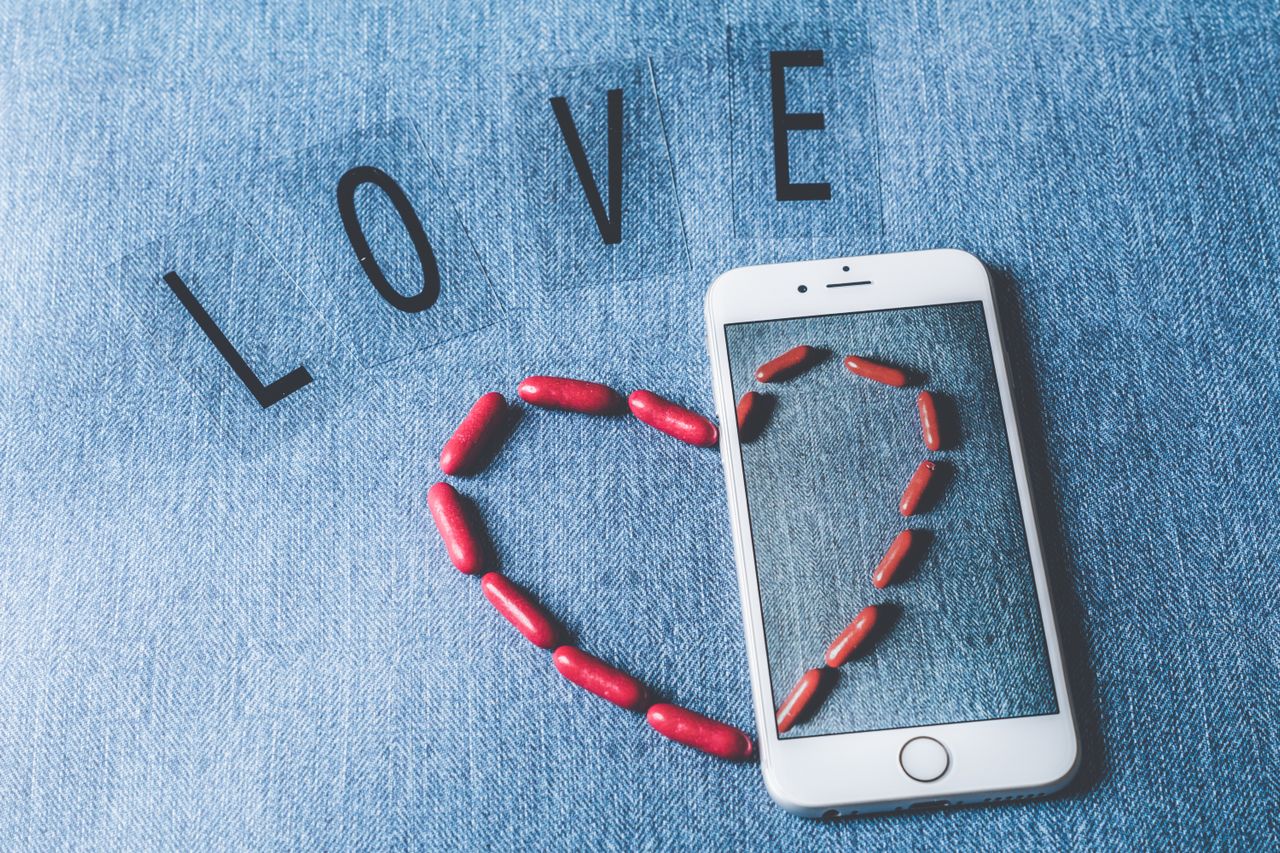 Red candy arranged in a heart on a smartphone, symbolizing love and technology