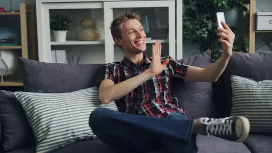 A man smiles and makes a video call while sitting on a gray couch