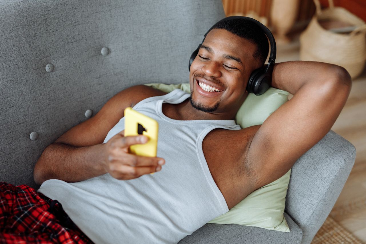 A man video chats with someone on his phone while lounging on a couch