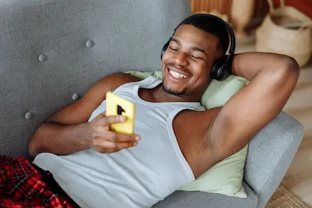 A man video chats with someone on his phone while lounging on a couch
