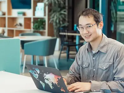 A man smiling while working on a laptop in a modern office