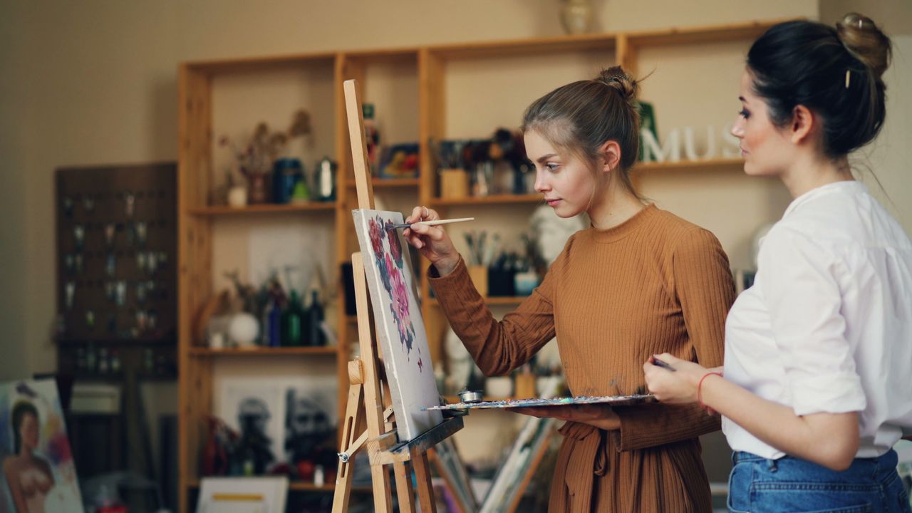 Two women concentrate on their hobby and paint on a canvas