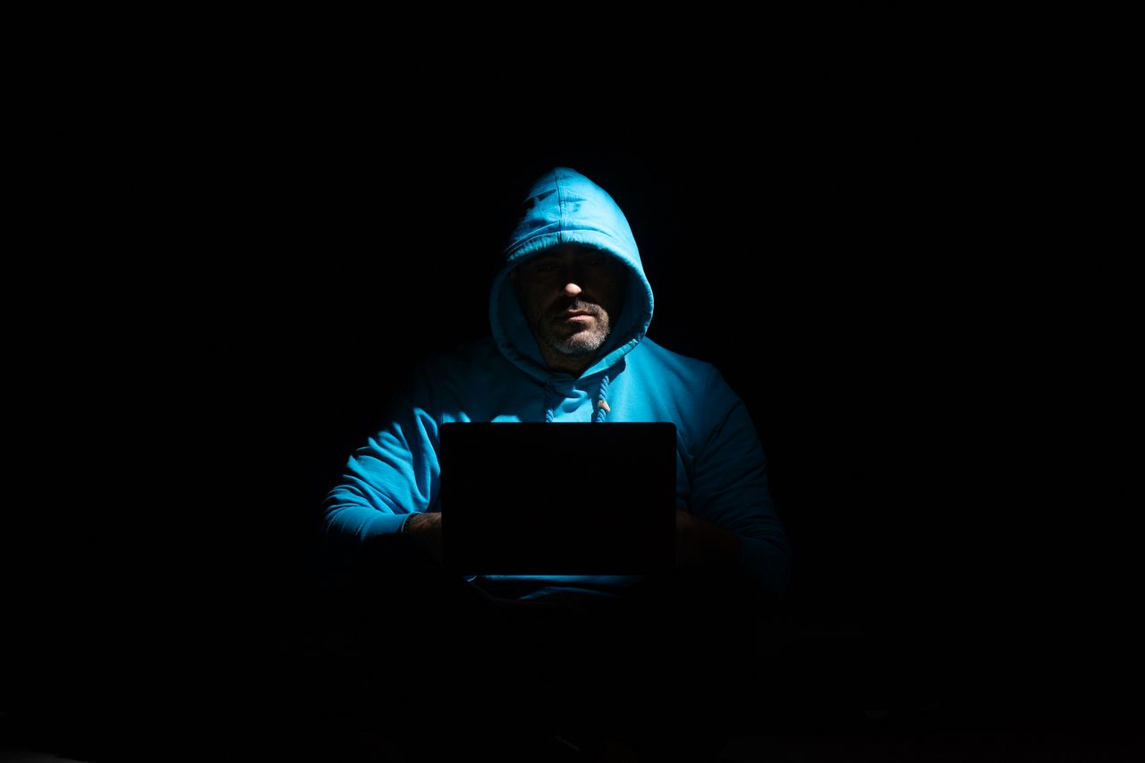 A suspicious man wearing a hoodie using a laptop in the dark
